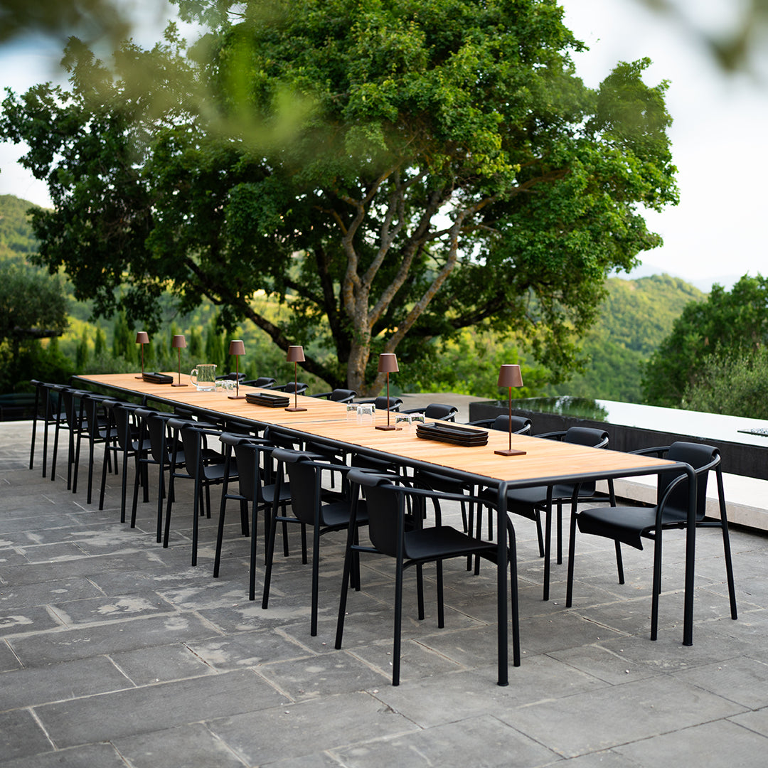 "Elegant black chairs and natural wood table set against a lush green backdrop, perfect for outdoor dining."