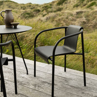 Black minimalist chair with smooth, matte finish against a natural backdrop of grass and wood. Perfect for outdoor settings.