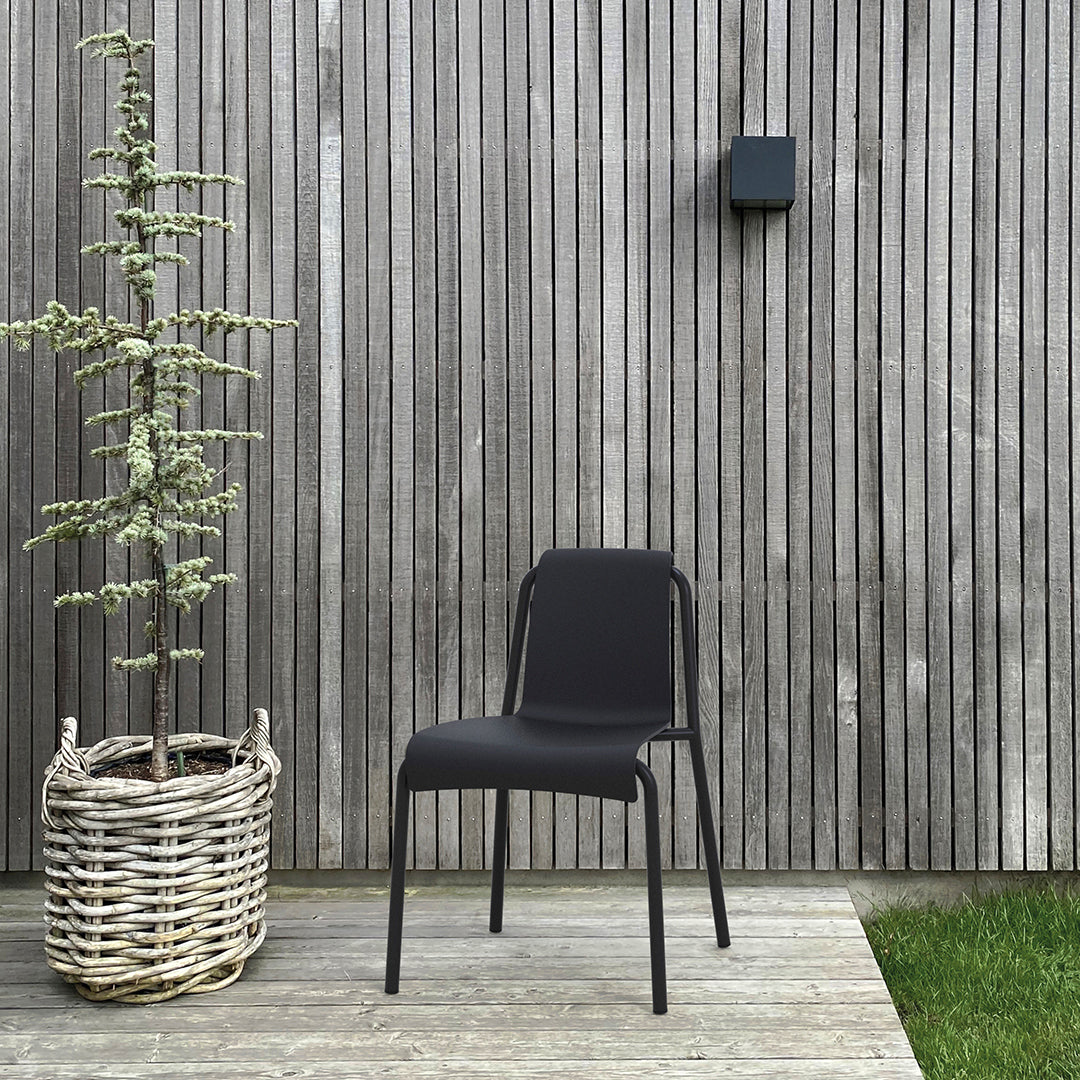 Stylish black chair with a sleek design, set against a wooden backdrop, paired with a textured basket and greenery.