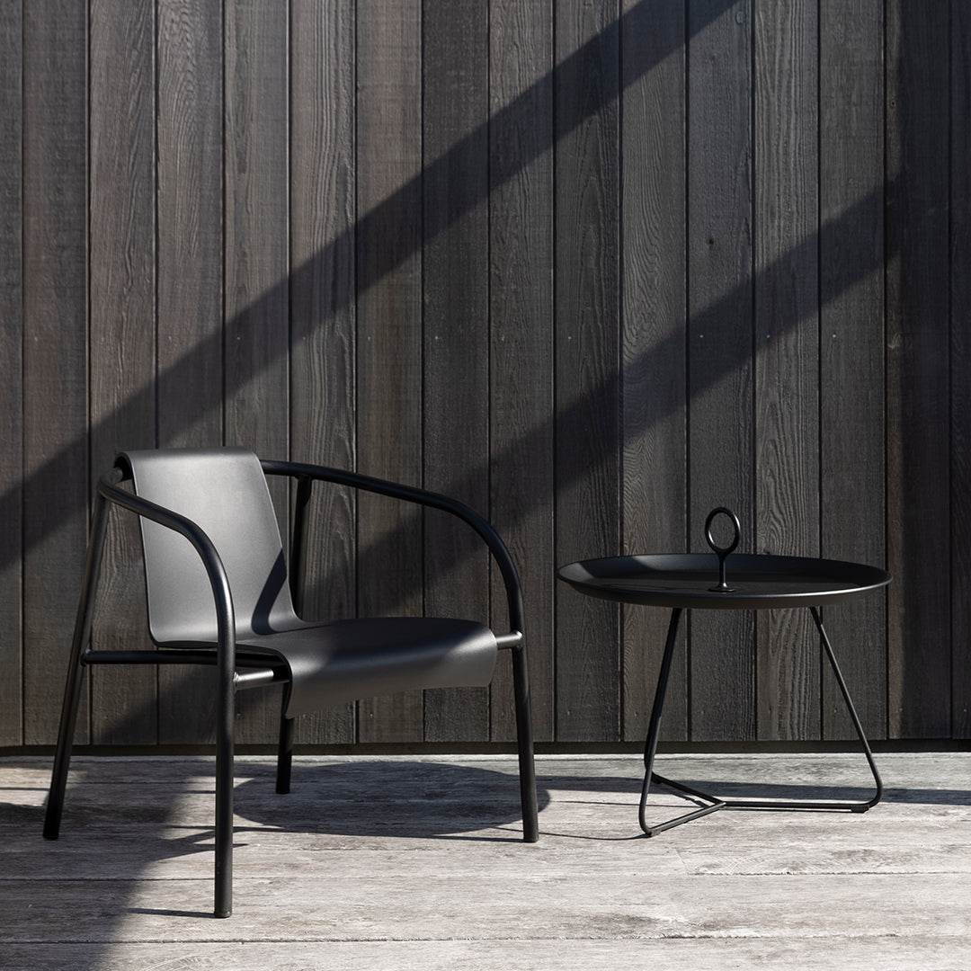 Black modern chair and round side table against dark wooden backdrop, sleek minimalistic design with clean lines.