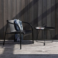 Black chair and round table with a checkered blue and gray throw blanket, against a dark wooden wall.
