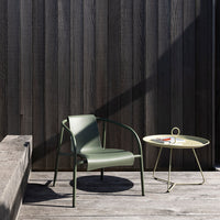 Green patio chair and round yellow side table against a dark wooden wall, showcasing modern colors and sleek design.