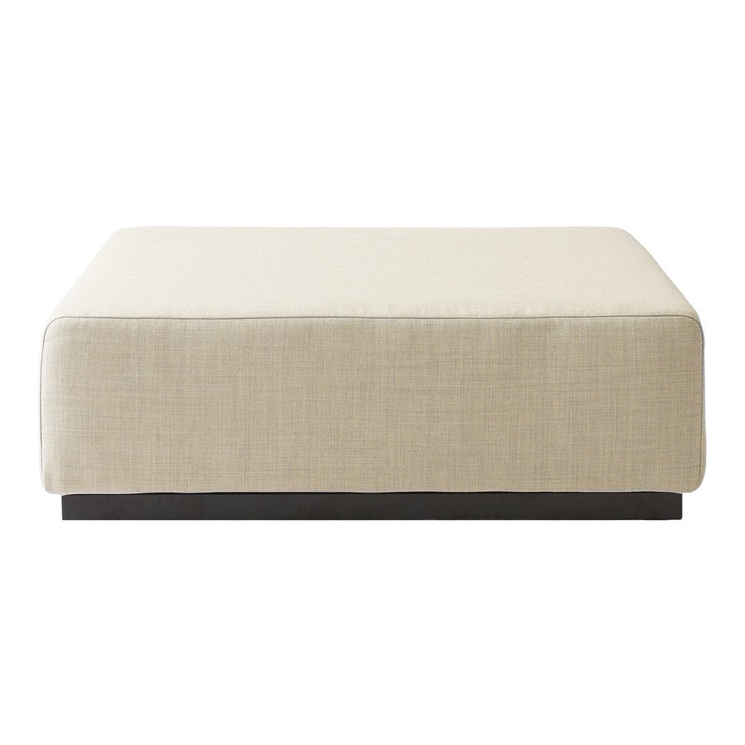 Light beige upholstered ottoman with a smooth texture and dark wood base. Modern, minimalist design.