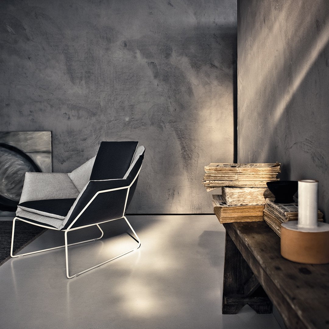 Modern lounge chair in black and gray, featuring sleek geometric lines and a minimalist design against a textured wall.