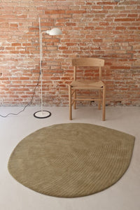 Beige textured rug in an organic leaf shape against a modern, minimalistic room with a warm brick wall.