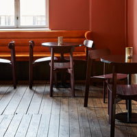 Cozy wood tables and chairs in warm brown tones against a rich, rust-orange wall with wooden flooring.