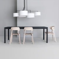 Modern black dining table with light wood chairs, featuring white cylindrical pendant lights against a gray backdrop.