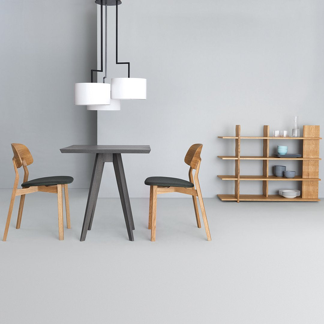 Modern gray dining table with light wood chairs and shelving, complemented by white pendant lights in a minimalist space.