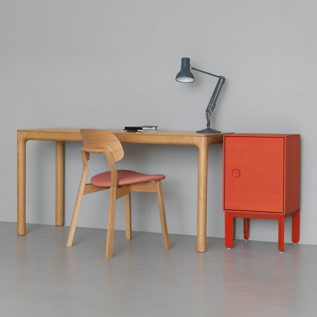 Light oak desk with soft pink chair, complemented by a bold orange cabinet against a neutral gray wall.