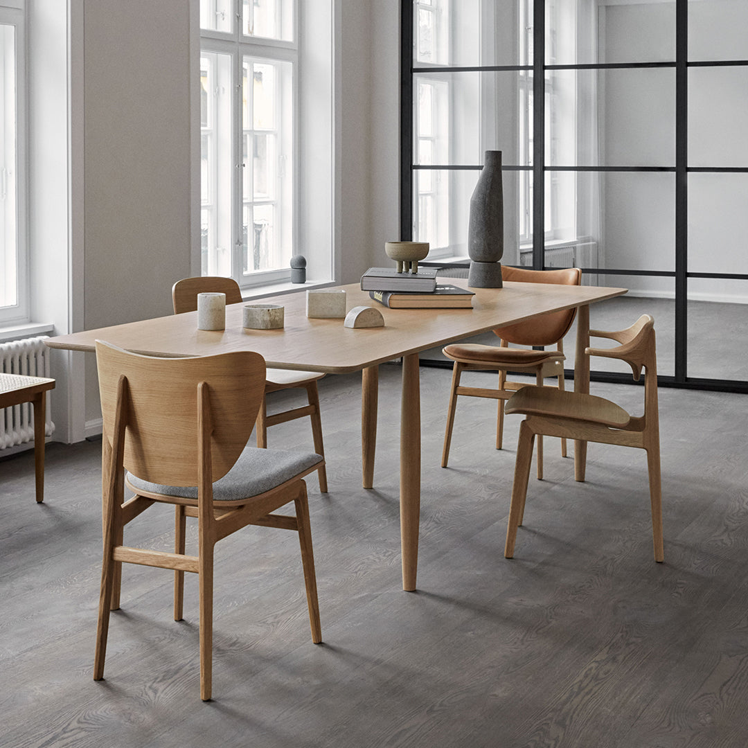 Light wood dining table with natural finish, complemented by soft grey upholstered chairs in a minimalist setting.