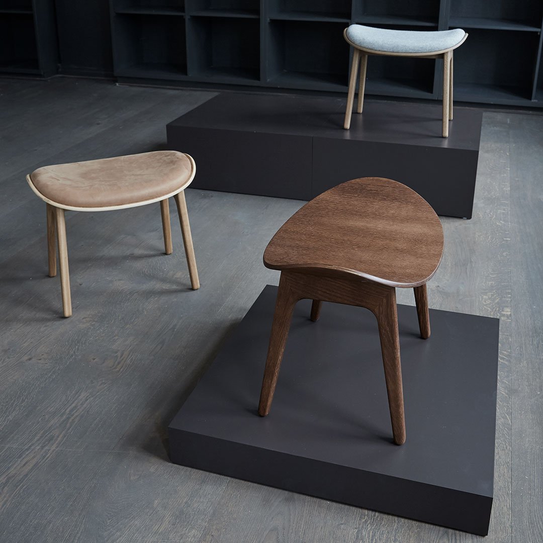 Three stylish chairs with natural wood textures: light beige, rich brown, and smooth white, displayed on dark stands.