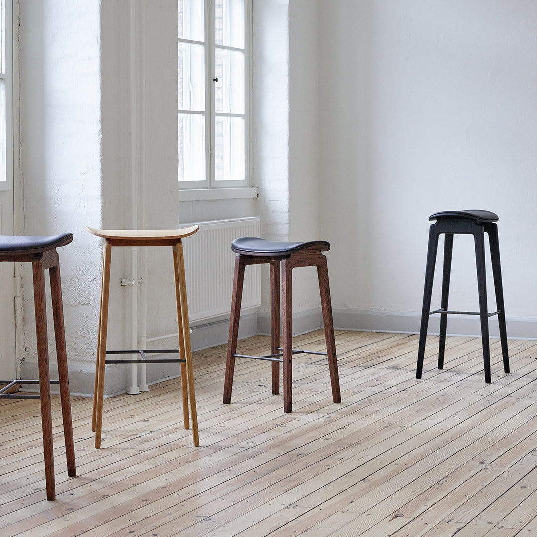 Set of four sleek bar stools in natural wood, featuring black, walnut, and light finishes on minimalist designs.
