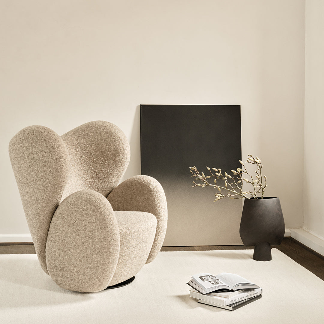 Modern beige upholstered chair with rounded edges, minimalist black wall art, and textured cream rug in a bright setting.