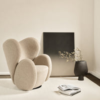Modern beige upholstered chair with rounded edges, minimalist black wall art, and textured cream rug in a bright setting.