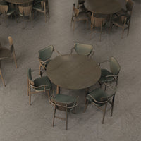 Round wooden table with a dark finish surrounded by green and beige patterned chairs on a gray floor.