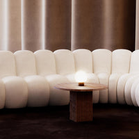 Curved white sectional sofa paired with a textured wooden coffee table on a dark brown rug. Soft, modern design.