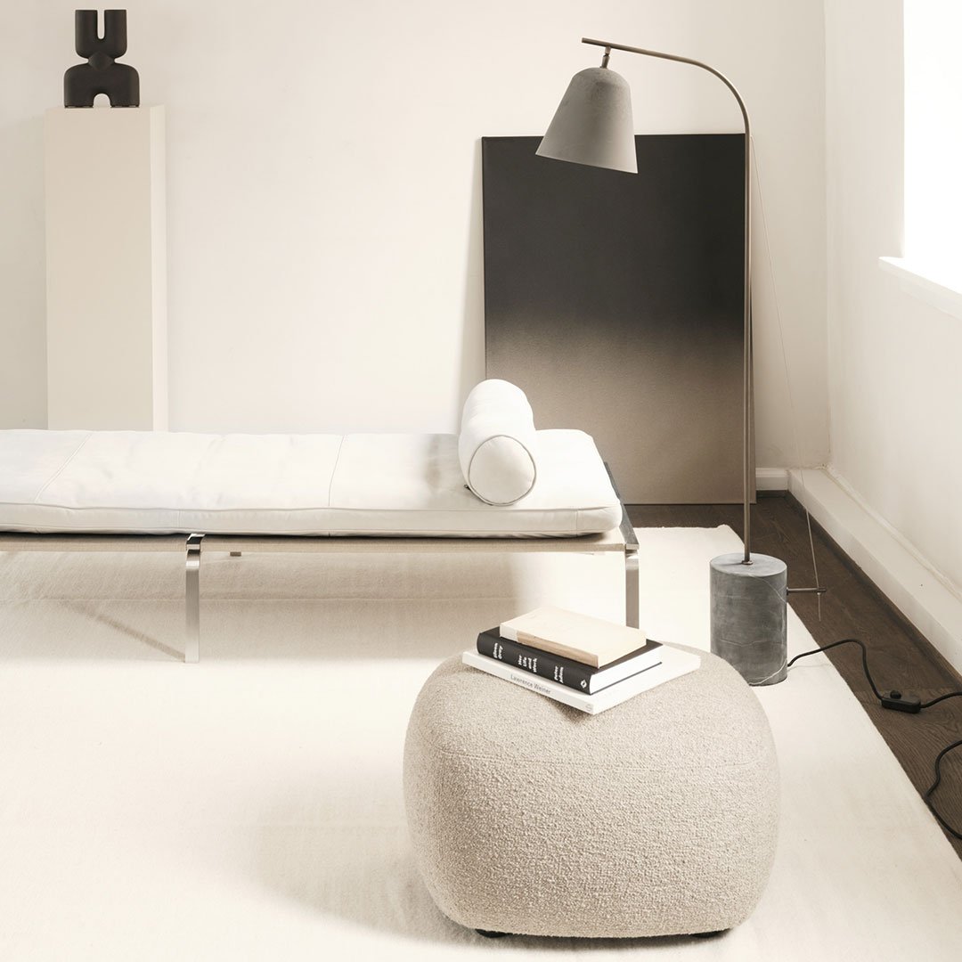 Soft beige pouf with a textured pattern, complemented by a sleek gray lamp and minimalist black accents.