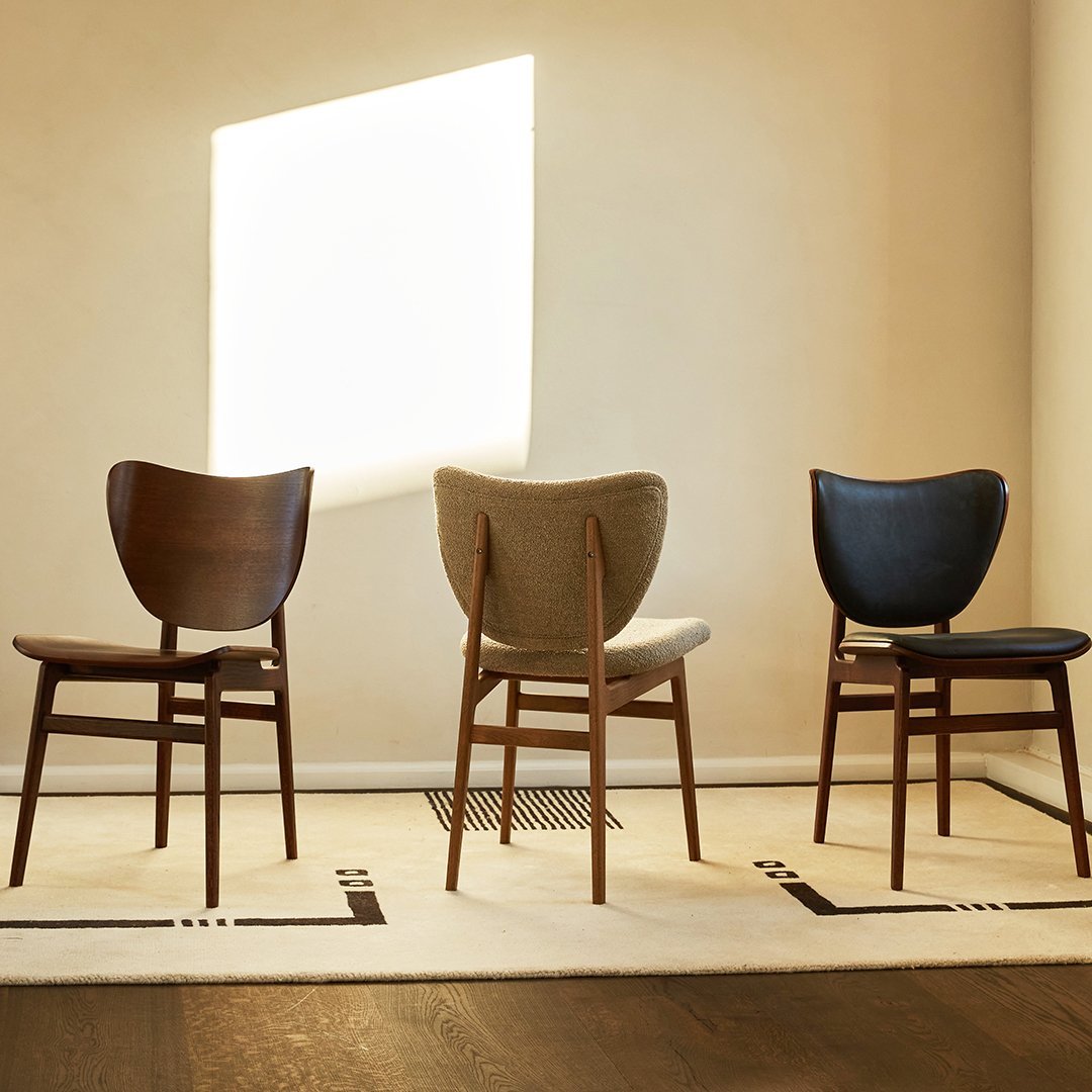 "Three stylish chairs in dark wood, beige, and black, arranged on a geometric patterned rug under soft natural light."