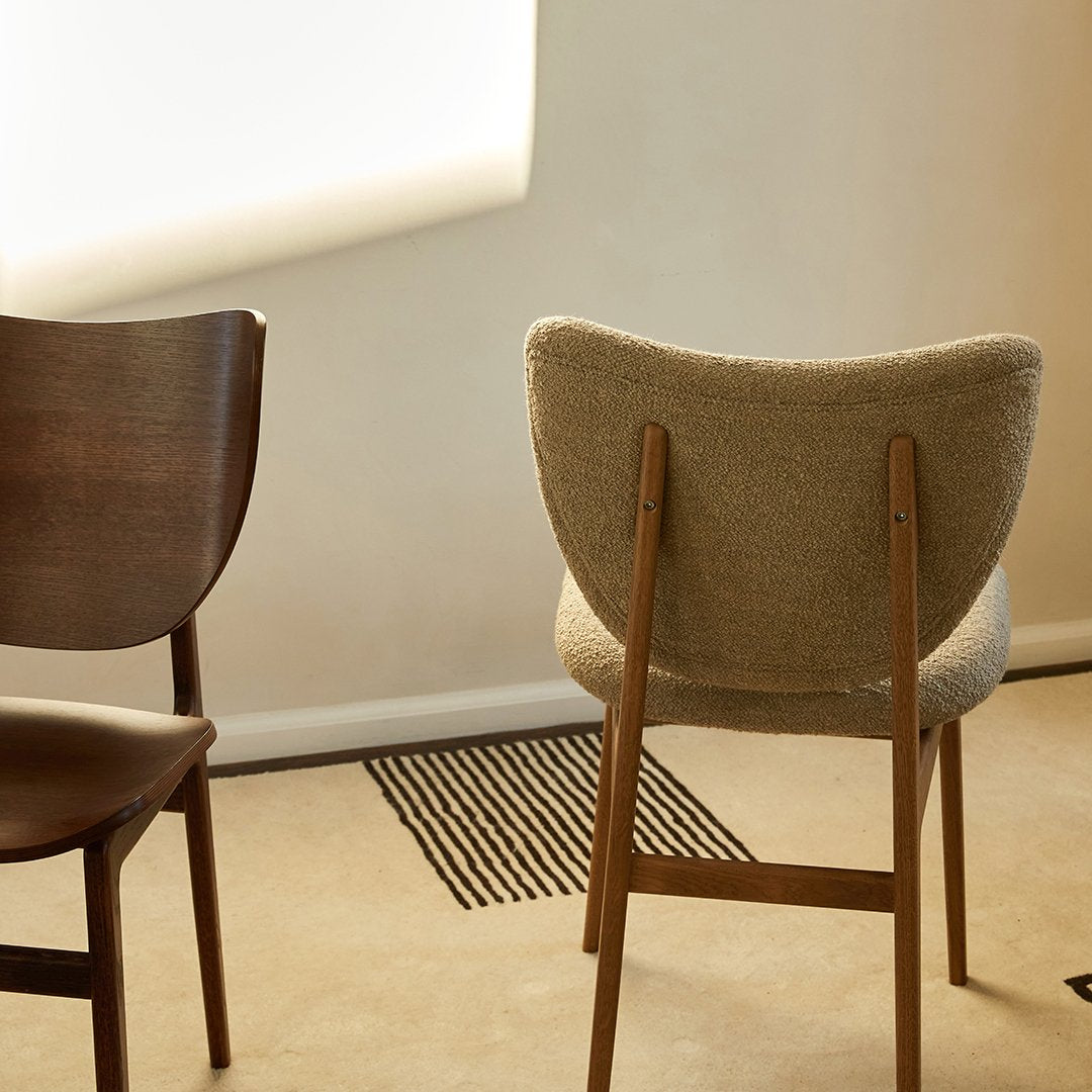 Wooden chairs in dark brown and light beige upholstery, set against a neutral background with geometric patterns on the floor.