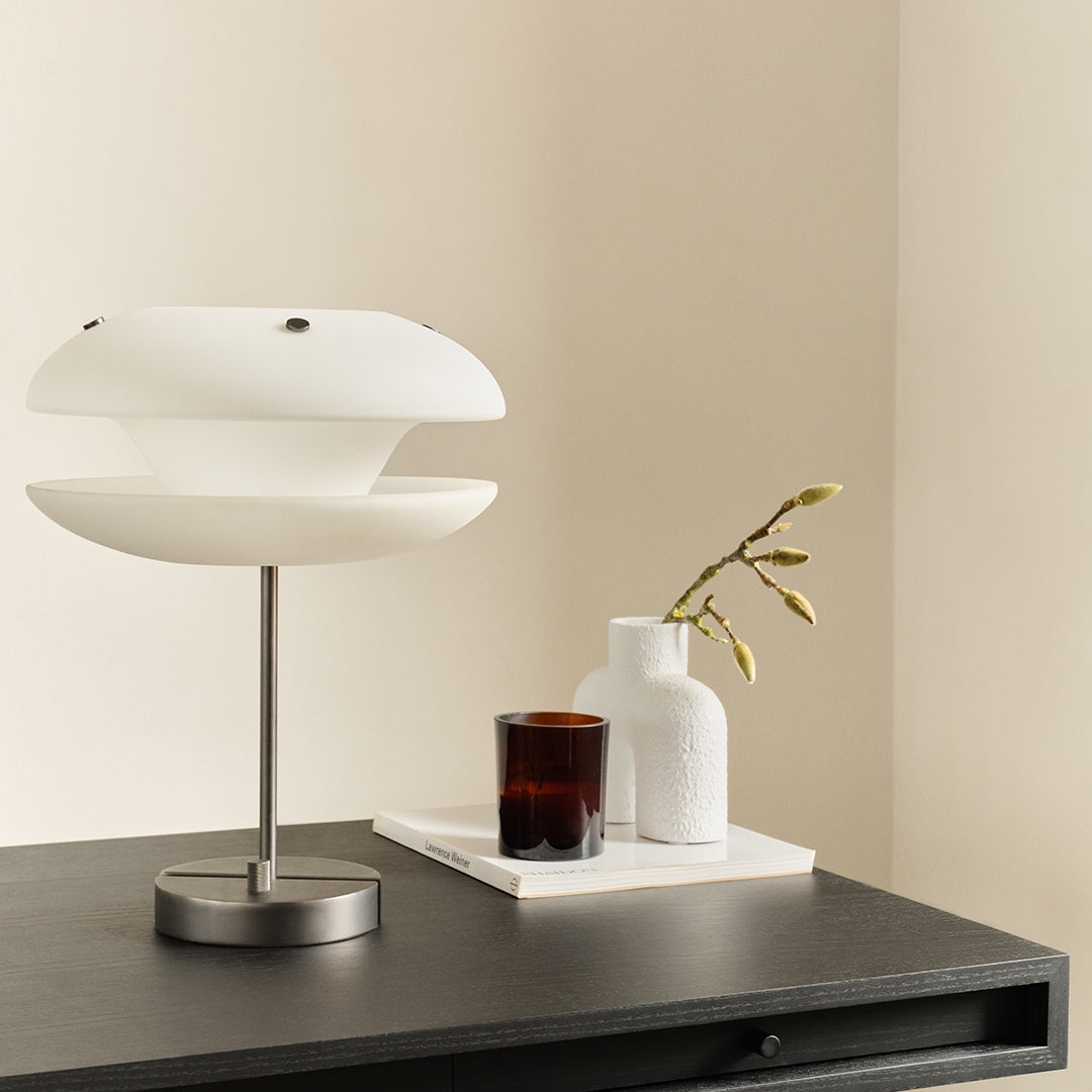 Contemporary white lamp with smooth curves, set against a neutral background and dark tabletop. Sophisticated, minimalist design.