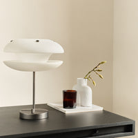 Modern white lamp with sleek curves, surrounded by a brown candle and minimalist white vases against a neutral backdrop.