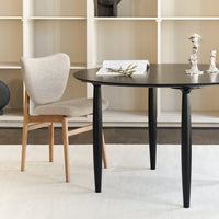 Modern black round table with sleek black legs and light gray upholstered chair against a neutral backdrop.