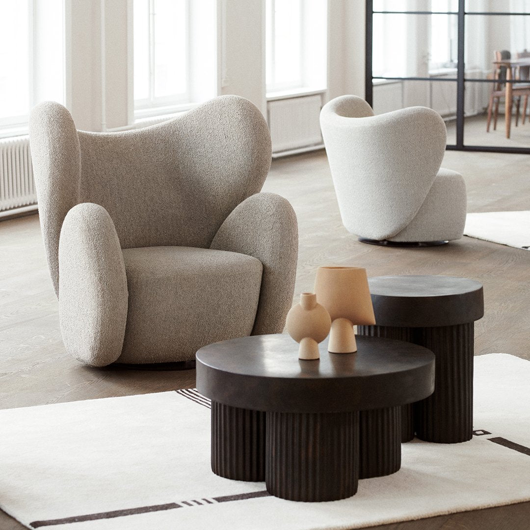 Gray textured armchair with curved silhouette; sleek black accent tables with ribbed pattern on a soft beige rug.