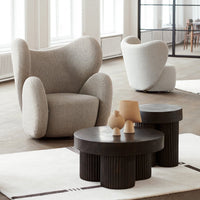 Gray textured armchair with curved silhouette; sleek black accent tables with ribbed pattern on a soft beige rug.