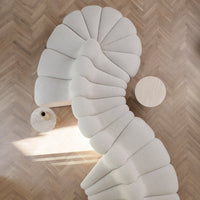 Cream-colored curved sofa with a unique fan pattern, paired with a light wood round side table on herringbone flooring.