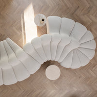 Curved white sofa with soft scalloped pattern, set on a light herringbone floor with a round side table.