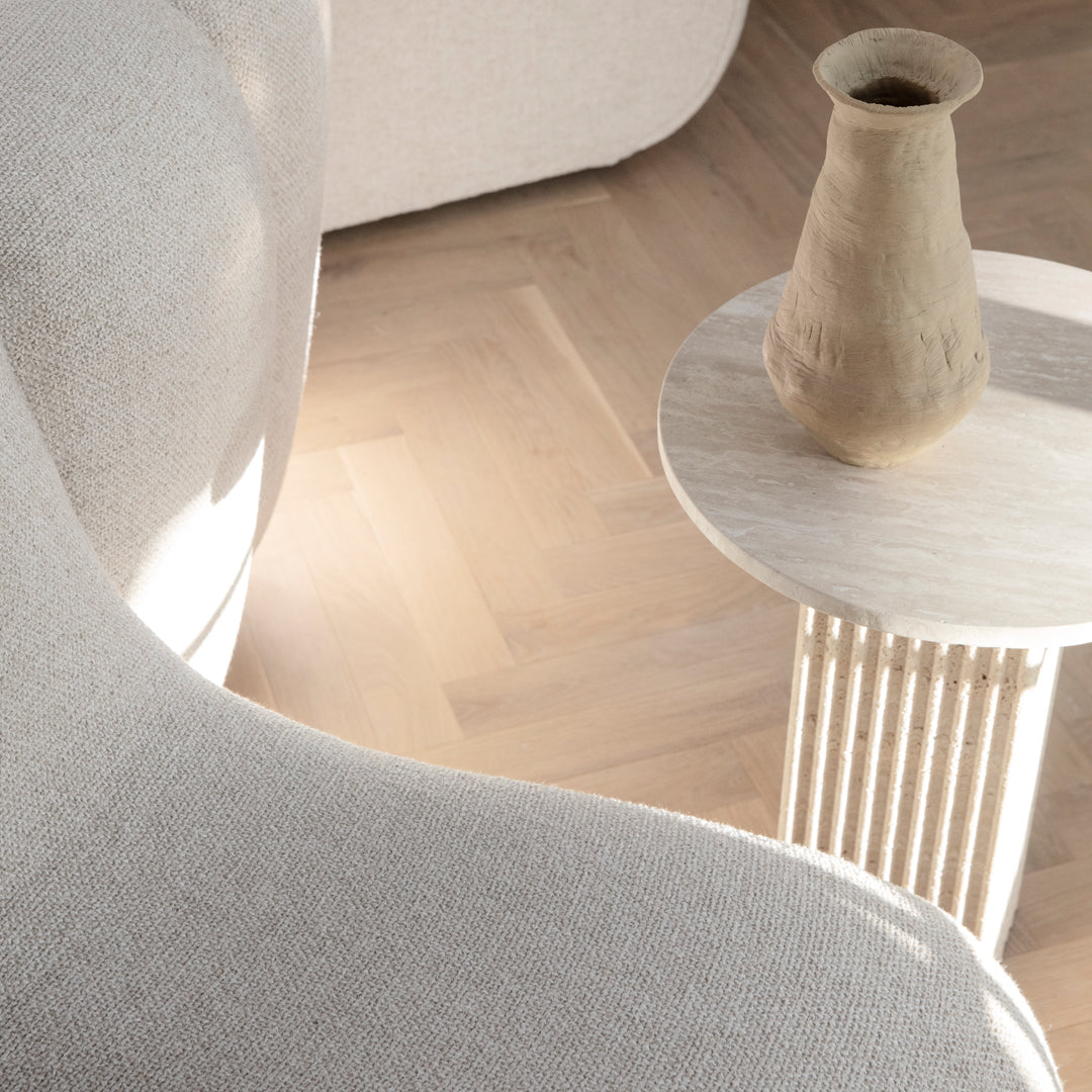 Soft beige textured fabric sofa with light wood flooring and a minimalist round table in neutral tones.