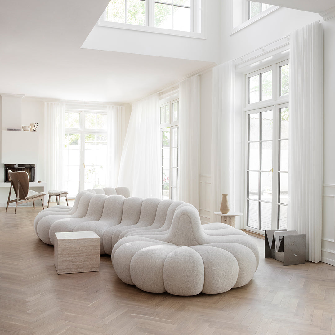 Curved white sofa with plush, textured fabric in a bright, airy room featuring natural light and wooden flooring.