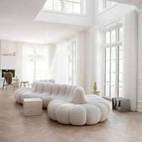White plush sofa with rounded, cloud-like design, set against a bright, airy room with natural wood flooring.