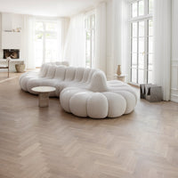 Elegant white sofa with plush, rounded shapes against warm herringbone wood flooring in a bright, airy room.