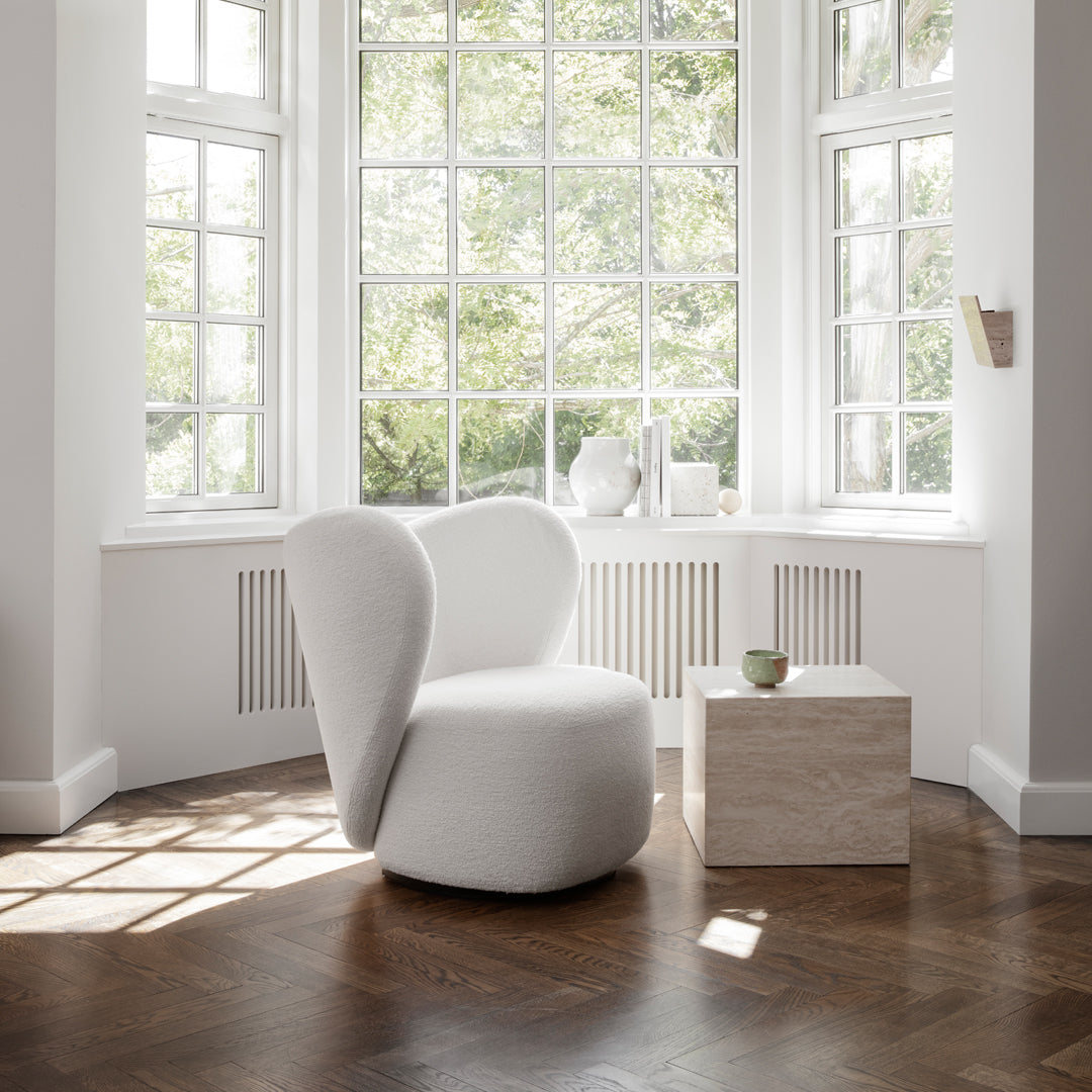 Soft white upholstered chair with smooth curves, paired with a light stone-colored side table on rich brown hardwood floor.