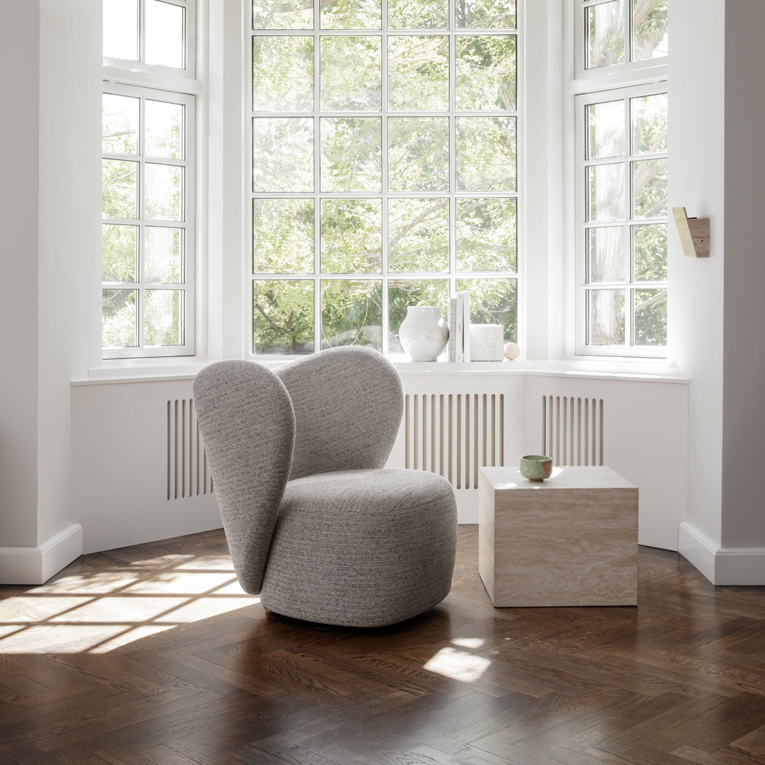 Textured light gray chair with rounded edges, paired with a smooth beige cube in a bright, sunlit room.