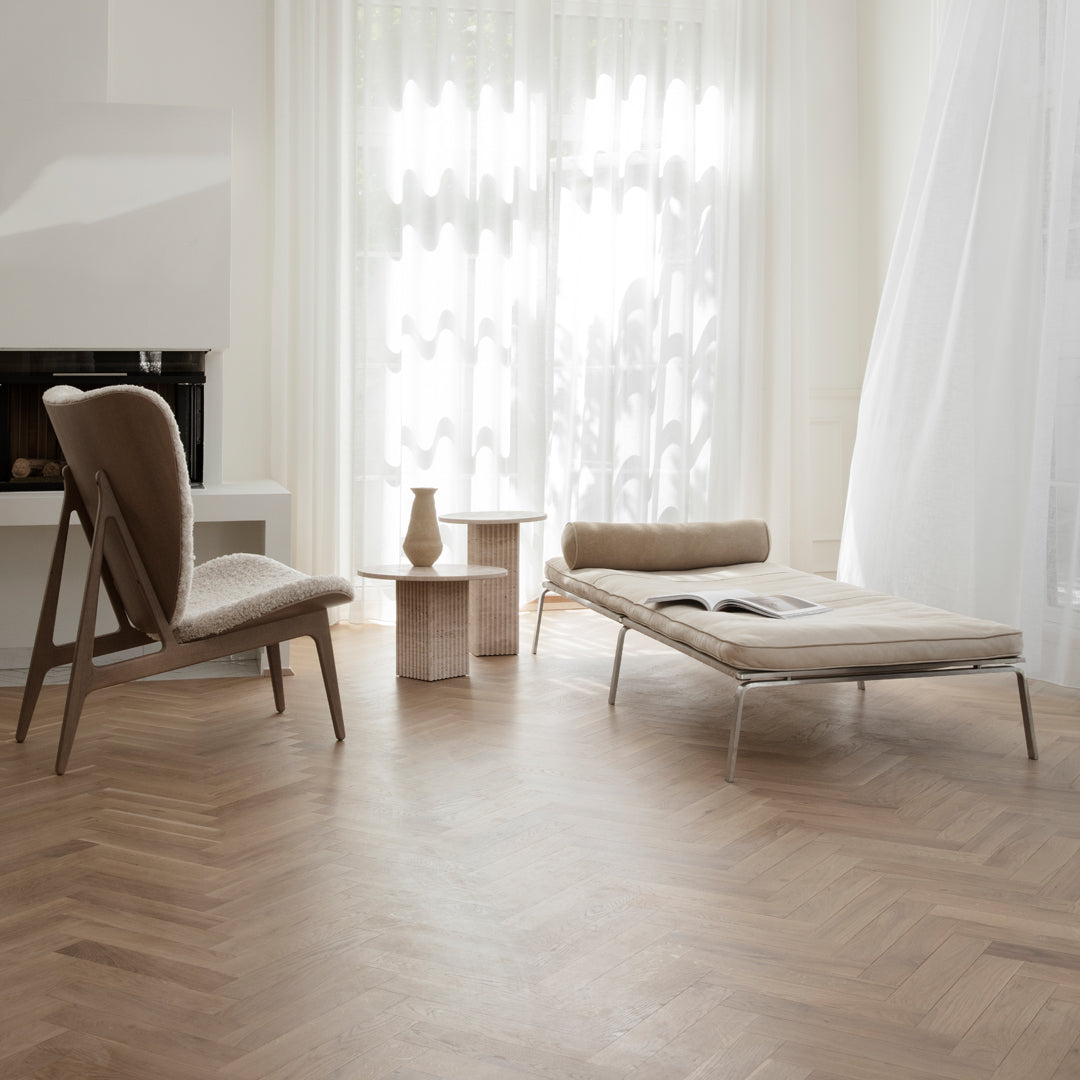 Modern beige lounge chair and cream chaise with light wood accents against a herringbone-patterned floor.