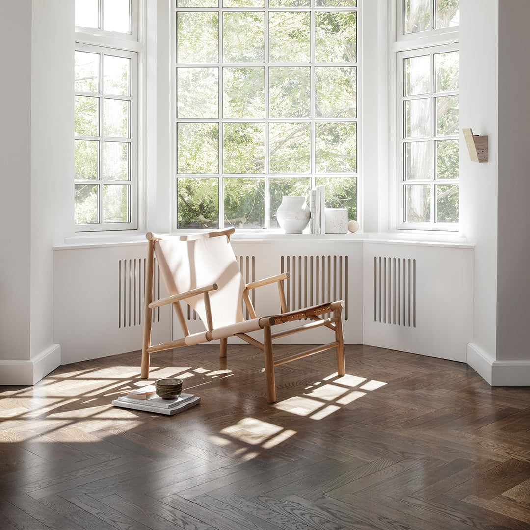Light wooden chair with natural canvas fabric in a sunlit room featuring white walls and herringbone wood flooring.