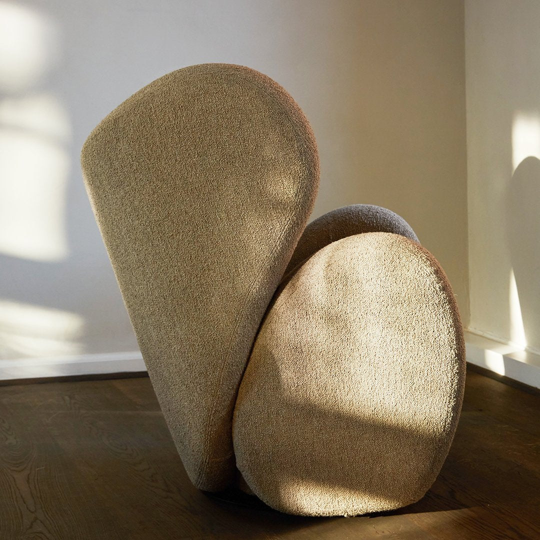 Beige sculptural chair with soft curves and a textured finish, set against a bright, sunlit background.