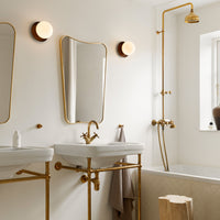 Elegant gold fixtures and mirrors against a neutral cream and white background create a stylish bathroom aesthetic.