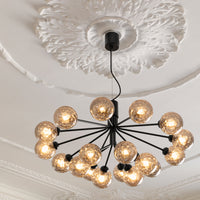 Black chandelier with 15 textured gold glass bulbs against a white, ornate ceiling. Elegant and modern design.