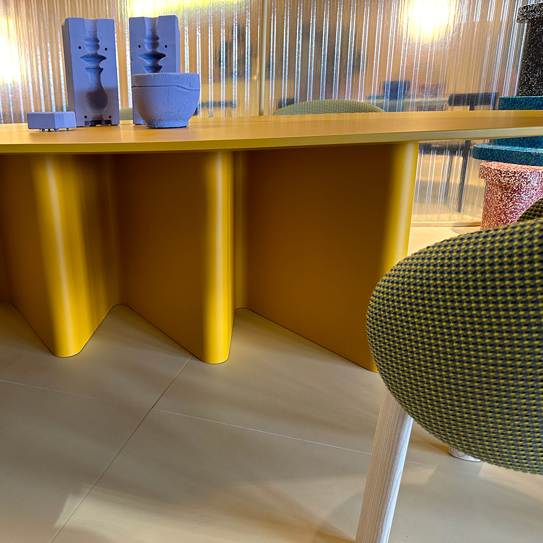 Yellow table with geometric design and textured green chair featuring a circular pattern. Minimalist decor accents in violet.