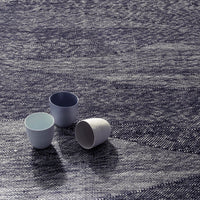 "Three ceramic cups in blue and white on a textured navy patterned surface."