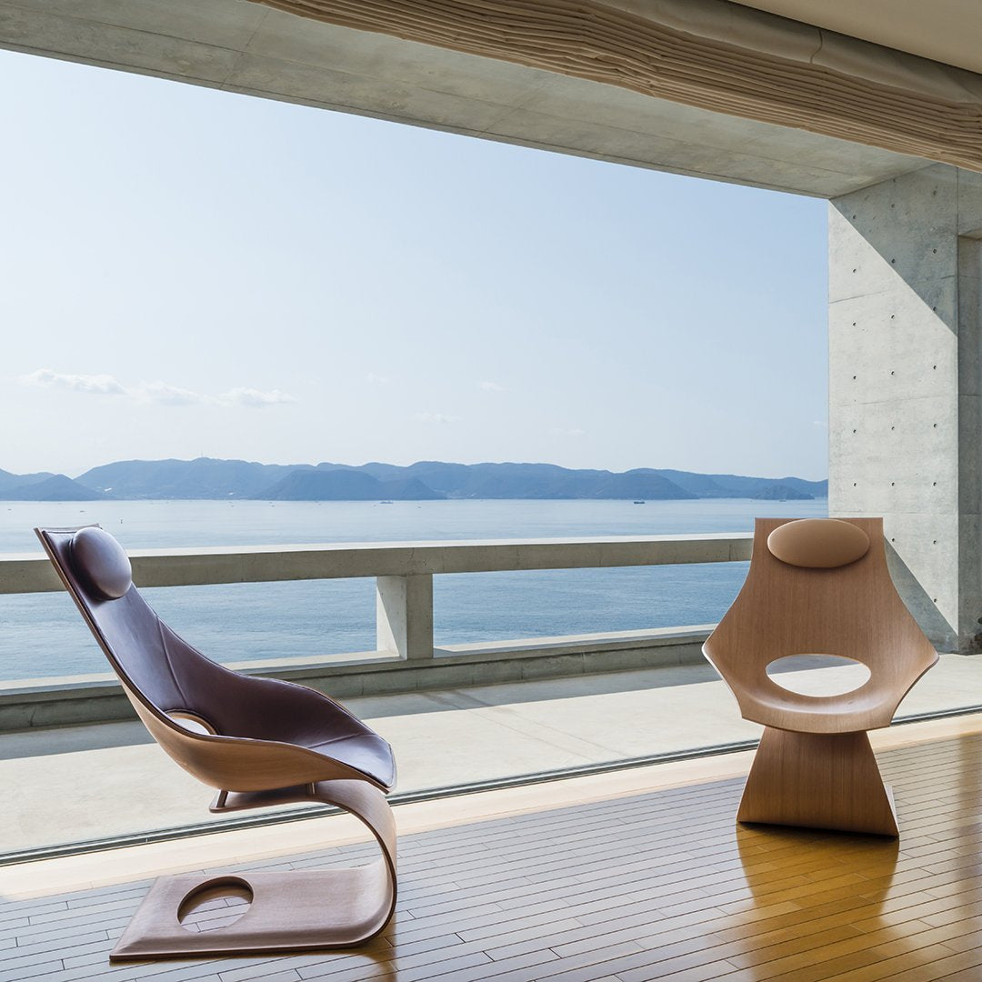 Modern wooden chairs with smooth curves, featuring warm hues of brown and beige against a scenic seaside backdrop.