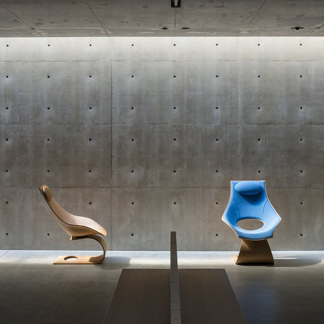 Modern chairs in natural wood and vibrant blue, set against a textured concrete wall and soft lighting.