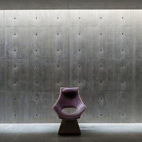 Modern chair in soft purple with a minimalist design, set against a textured concrete wall and dim lighting.