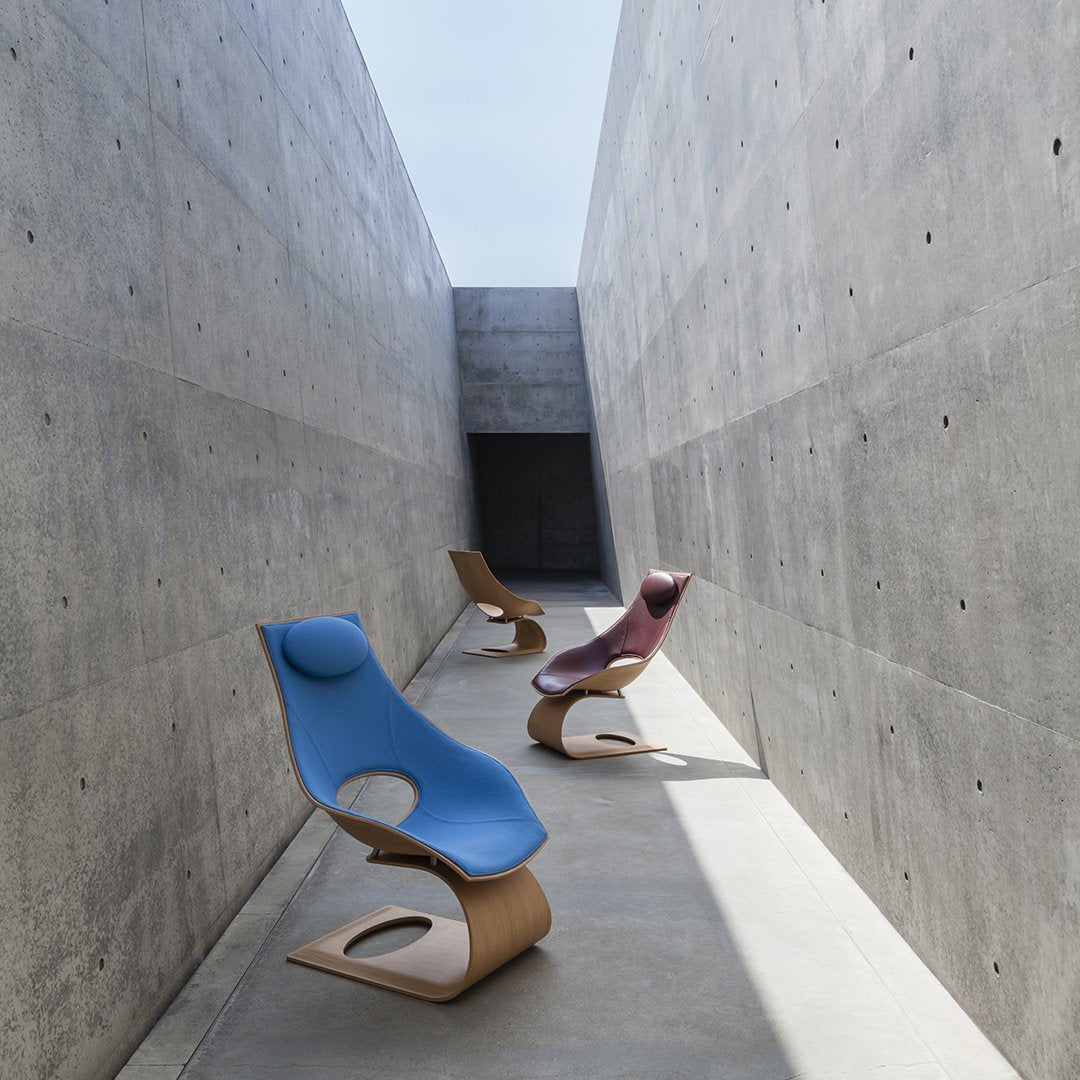 Curved lounge chairs in blue, burgundy, and natural wood, set against a minimalist concrete backdrop.