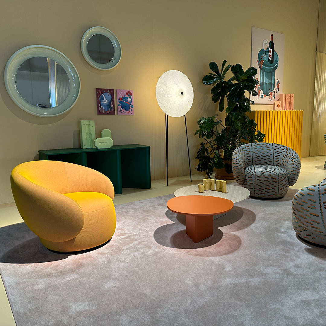 Modern living room with a yellow-orange chair, green accents, and patterned cushions on a soft gray rug.