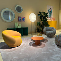 Modern living room with a yellow-orange chair, green accents, and patterned cushions on a soft gray rug.