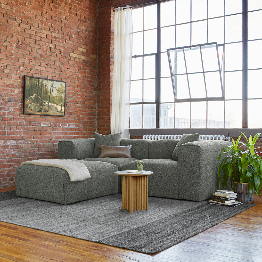 Gray fabric sectional sofa with textured cushions and a light gray throw on a striped gray area rug.